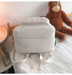 Off-white faux leather backpack with mesh side pockets on a bed with a plush toy