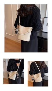 Detail of cream bucket bag featuring a woven handle, rabbit charm, and litchi texture PU leather