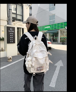 White nylon backpack with multi-pocket design and cute bear pendant in street scene