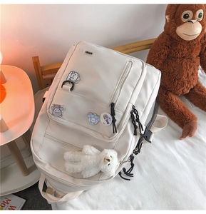 Detailed view of white large capacity school backpack with cute badges and teddy pendant