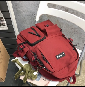 Detail of red canvas school backpack featuring multi-pocket design and green frog charm