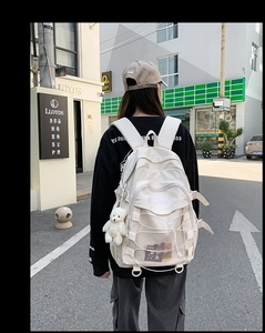 Detail of cream white nylon backpack with multiple compartments and bear charm accessory