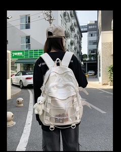 Outdoor shot of a cream multi-pocket nylon backpack featuring decorative cross ropes