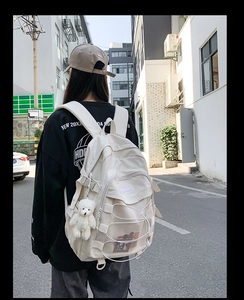 Outdoor shot of a cream campus backpack with criss-cross ropes and a cute plush bear charm