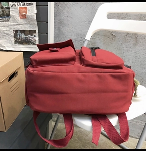Detail view of burgundy canvas backpack with multi-pocket design on modern white chair