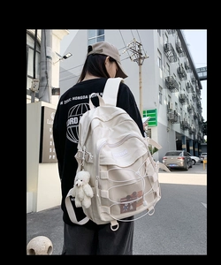 Detail view of the cream white backpack featuring a mesh pocket and plush bear pendant