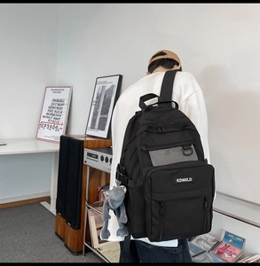 Detail view of black high-capacity backpack with KDMILD label and plush doll charm