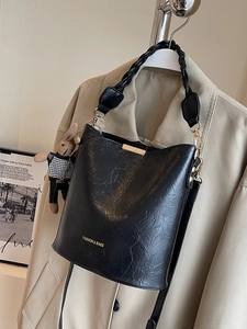 Fashionable black bucket bag with pleated texture and cute rabbit charm on tan blazer