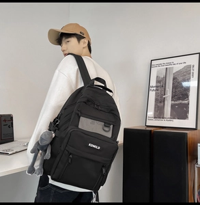 Male student wearing black multi-pocket backpack with KDMILD logo and frog charm
