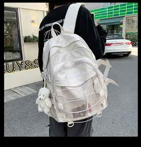 Detail view of cream functional backpack featuring multiple pockets and a plush bear charm
