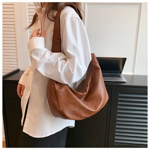 Detail of a large brown hobo bag showing high-quality leather texture and strap on a model