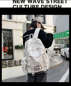 Street view of a cream-white college style backpack with cross cords and bear pendant