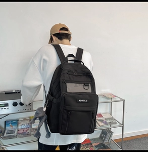 Detailed back view of a black multi-pocket backpack with a cute frog plush pendant charm