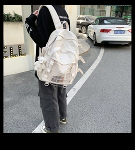 Detail view of cream nylon backpack with criss-cross ropes and a cute bear keychain