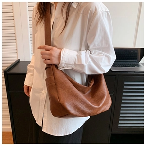 Detail view of a large dark brown faux leather crescent tote bag worn over the shoulder