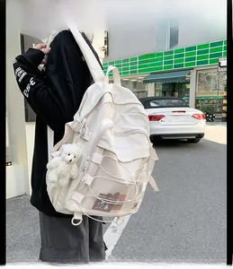 Detailed view of white college backpack with cross-rope mesh pocket and plush bear charm