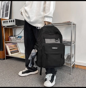 Detail view of large capacity black backpack featuring mesh pockets and cute plush pendant