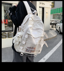 Detail of off-white canvas backpack featuring decorative cross cords and plush bear charm