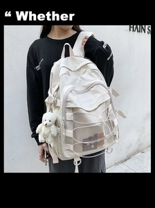 Detail of a creamy white backpack with mesh pockets, elastic cords, and a cute bear charm