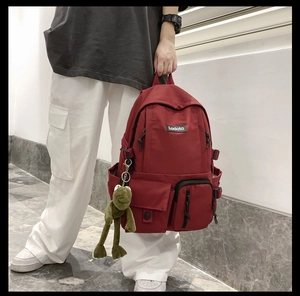 Detail view of red nylon backpack featuring multiple pockets and a green plush frog pendant