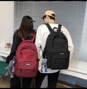 Close-up of burgundy and black backpacks with multi-layered pockets and plush charms