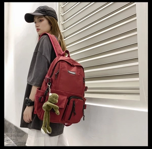 Outdoor shot of a red multifunctional school backpack with a cute frog plush pendant detail