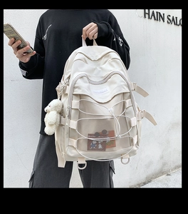 Detail view of cream canvas backpack with mesh pocket, elastic cords and plush bear charm