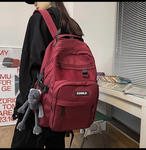 Detail view of burgundy multi-pocket nylon backpack with a cute grey frog plush keychain