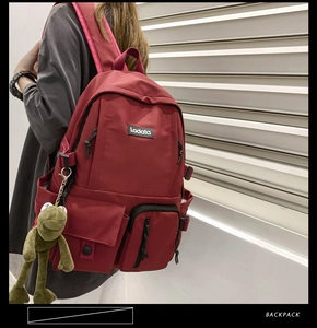Detail view of burgundy waterproof nylon backpack with multi-pocket design and cute charm