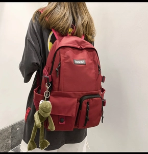 Detail view of burgundy canvas backpack with multiple pockets and green frog plush charm
