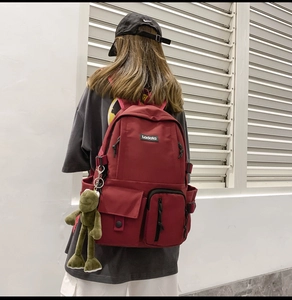 Detail of dark red canvas backpack with multiple pockets and a cute green frog keychain