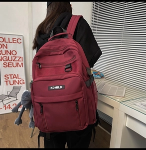 Detail view of burgundy backpack with multiple zippers and grey frog plush toy accessory