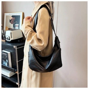 Model wearing a large black crescent tote bag with soft leather pleats and a wide strap