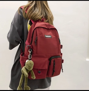 Detail view of burgundy nylon backpack with multi-pocket design and green frog pendant