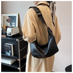Black crescent tote bag with leather texture shown on model wearing a beige trench coat