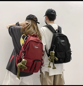Rear view of school backpacks in black and burgundy with plush frog keychain charms