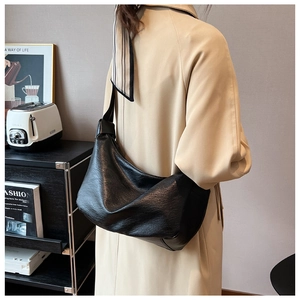 Detail of a large black faux leather tote bag worn with a stylish beige trench coat