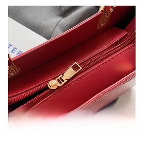 Detail shot of smooth gold-tone metal zipper on red embossed leather tote bag
