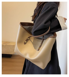 Detail view of large beige tote bag with brown straps and golden rivet accents