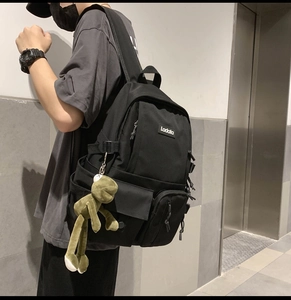 Detail of black nylon backpack with multiple pockets and a green plush frog accessory