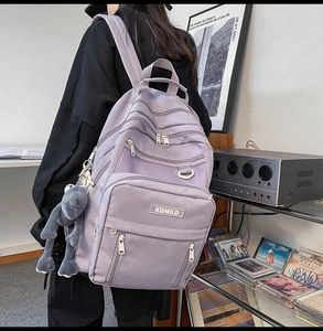 Detailed side view of lavender nylon backpack with multiple zipper pockets and plush charm