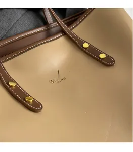 Detail of khaki leather tote with dark brown strap, contrast stitching and gold rivets