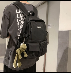 Close-up of black multi-pocket student backpack with a cute green frog charm