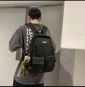 Detailed back view of a black canvas backpack with multi-pockets and green plush charm