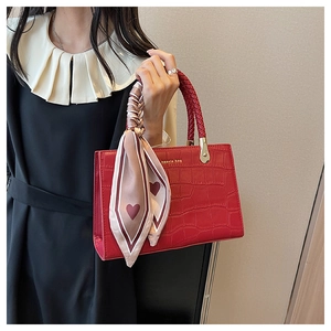 Detail of red crocodile embossed tote bag with woven handle and heart print silk scarf