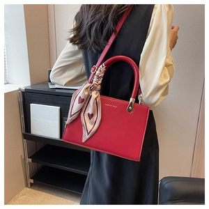 Detail of red leather tote bag with elegant silk scarf wrapped around handle and gold logo