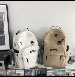 Detail of multi-pocket nylon backpacks in white and khaki with cute plush frog charms