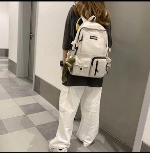 Rear view of a cream canvas school backpack with multiple pockets and a green frog charm
