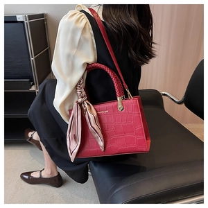 Close-up of red crocodile-embossed tote bag with woven handles and a decorative silk scarf