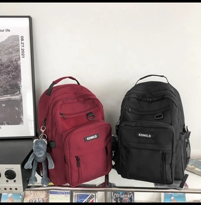 Close-up of burgundy and black student backpacks with multiple layers and frog pendant